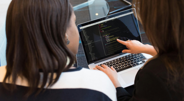 two women looking at computer that has lines of code on it